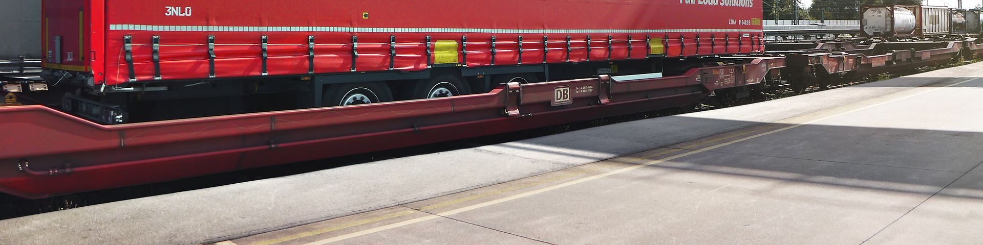 Ein kranbarer Trailer von DB Cargo FLS wird von einem Kran verladen.