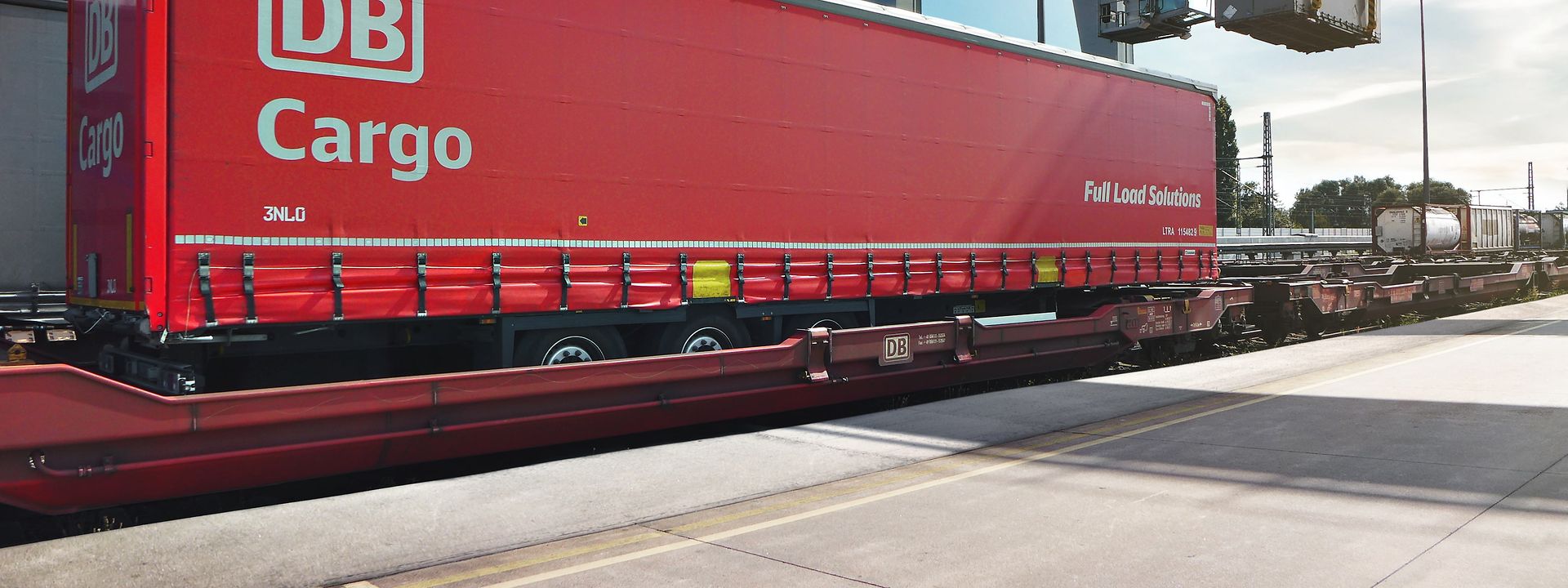 Ein kranbarer Trailer von DB Cargo FLS wird von einem Kran verladen.